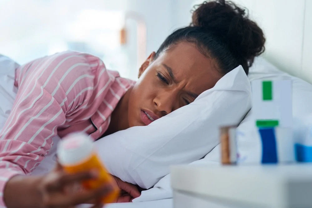 types-of-opioid-drugs a woman laying in bed holding a bottle of opioids