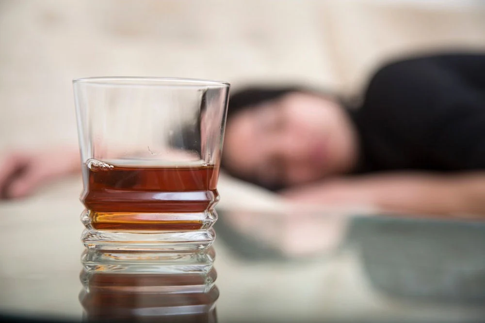 a woman laying down with glass of whiskey
