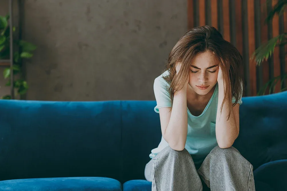 girl sitting on couch holding her head, struggling with anxiety disorder
