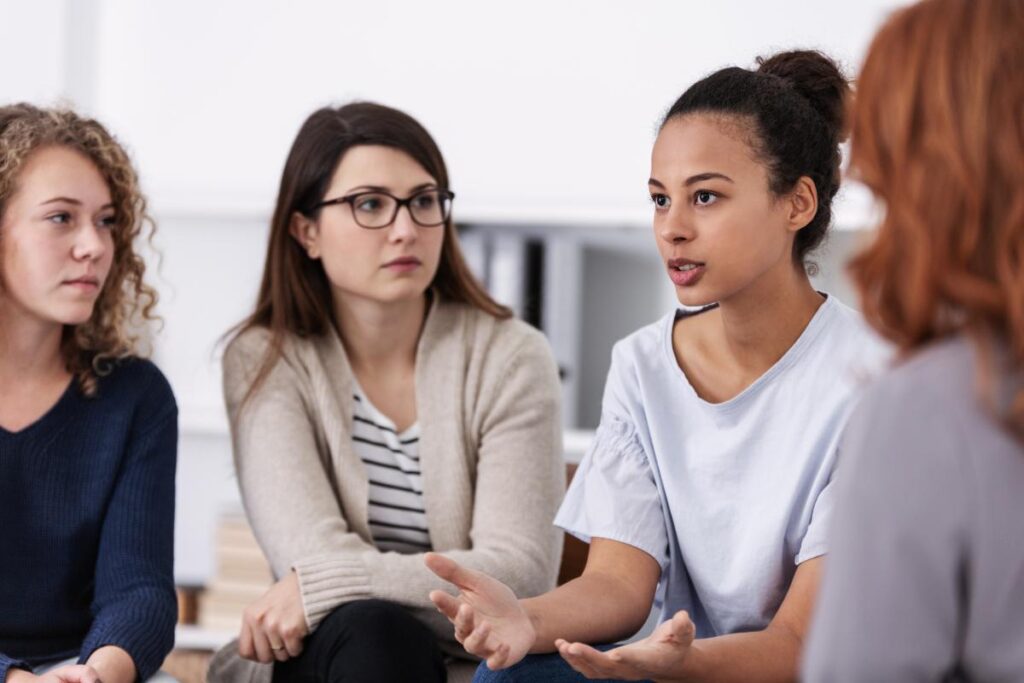 a group of women sit in chairs and talk about issues in a women's rehab