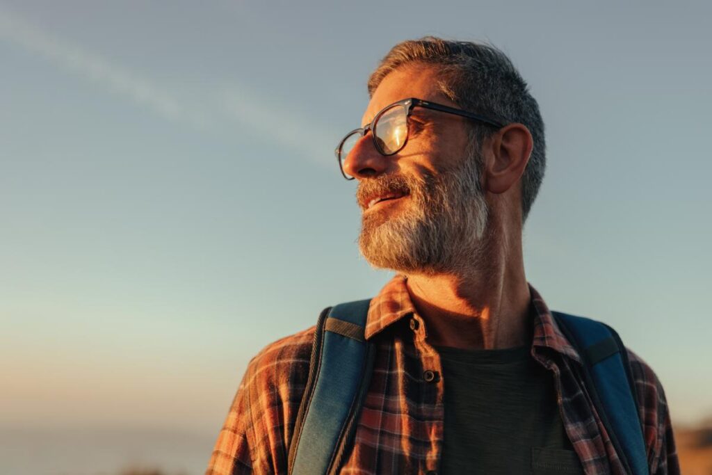 a man with glasses stands outside with a backpack on after completing a men's rehab